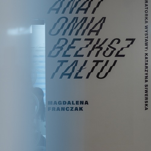 Tytuł wystawy na białej ścianie.