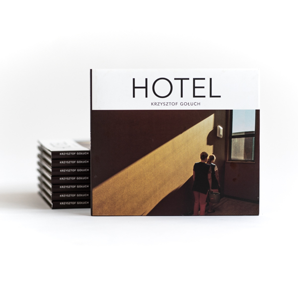 Okładka książki „HOTEL” Krzysztofa Golucha z fotografią dwóch osób idących korytarzem w promieniu światła.