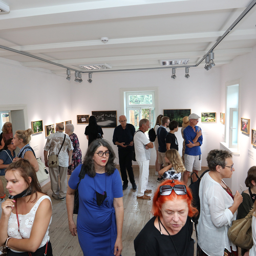 Grupa osób ogląda fotografie prezentowane na ścianach galerii podczas wernisażu.