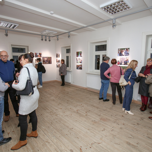 Grupa osób rozmawia i ogląda fotografie podczas wernisażu.