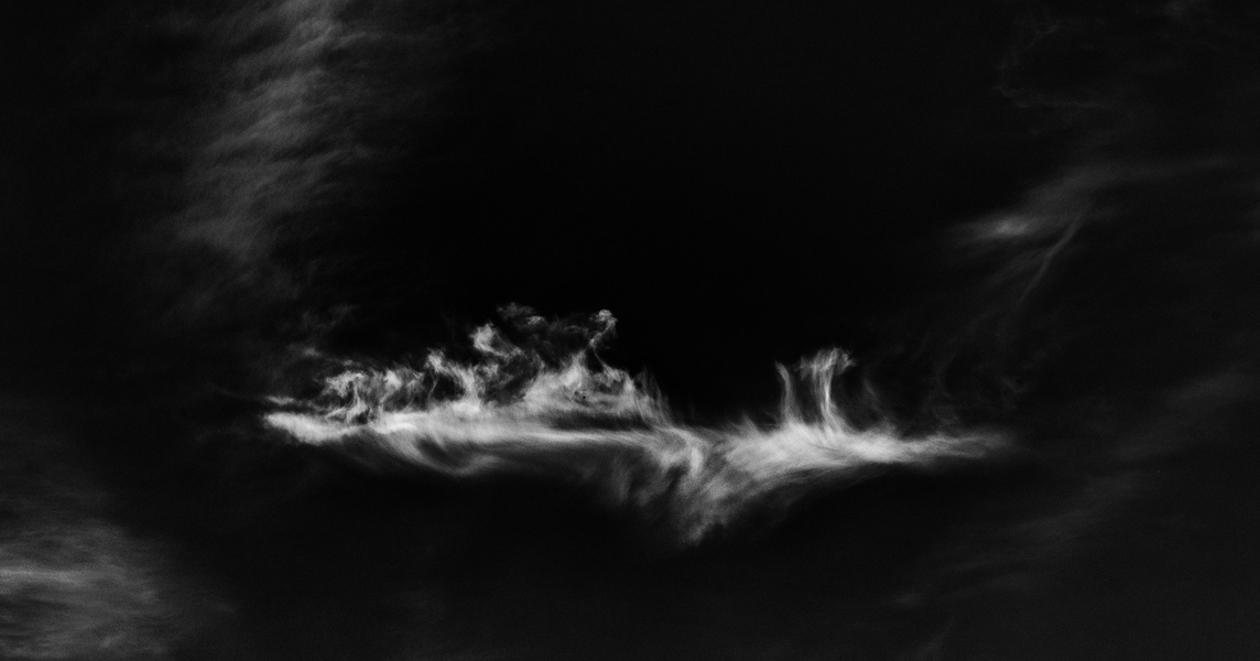 Czarno biała fotografia cyfrowa z białą chmurą na czarnym tle nieba.